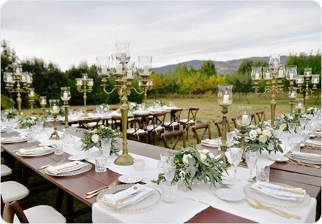 Luxe buitentafel voor een bruiloft met gouden kandelaars, witte bloemen en uitzicht op de bergen.